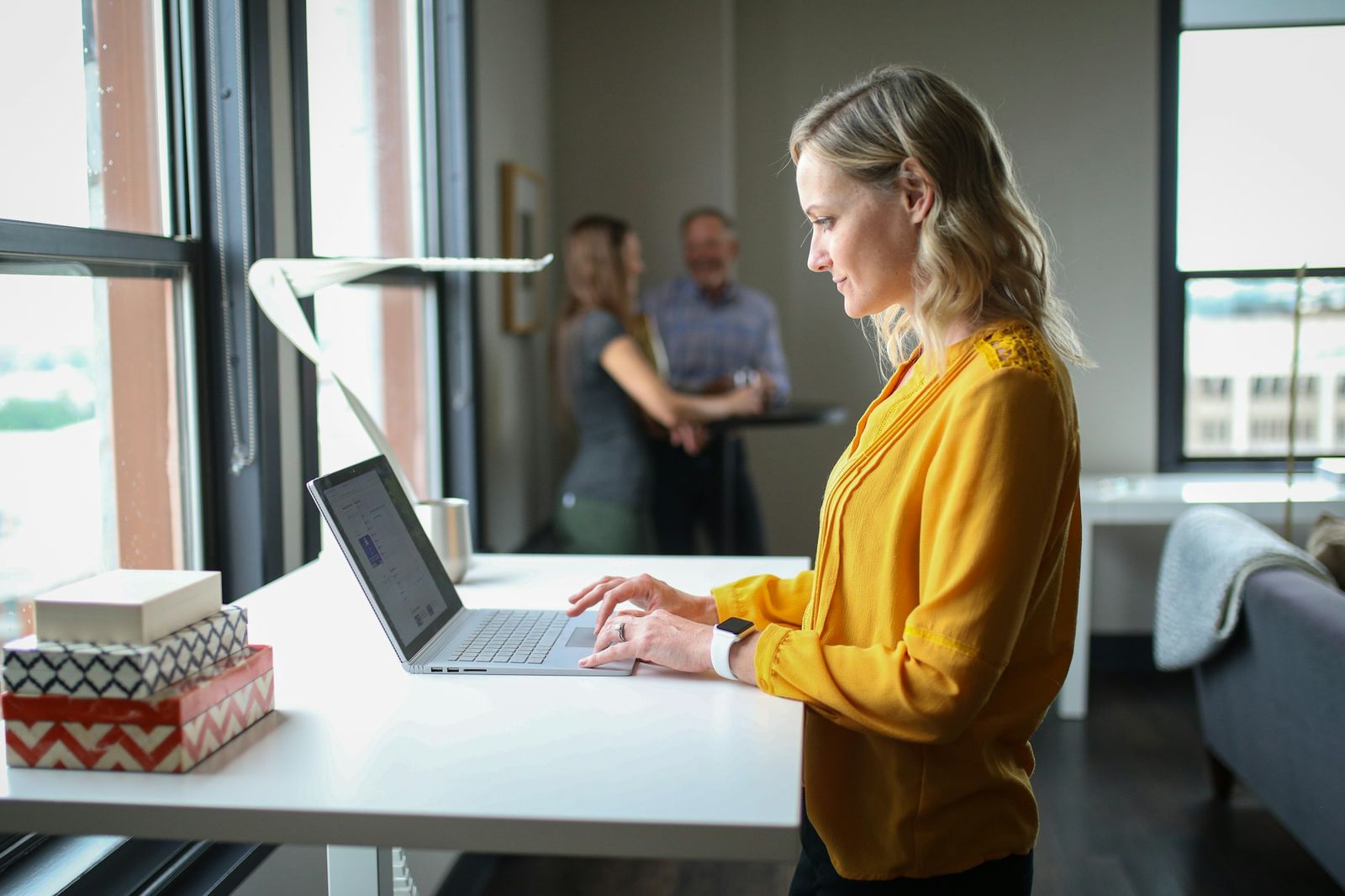 Professional working at a standing desk in a modern office with colleagues in the background